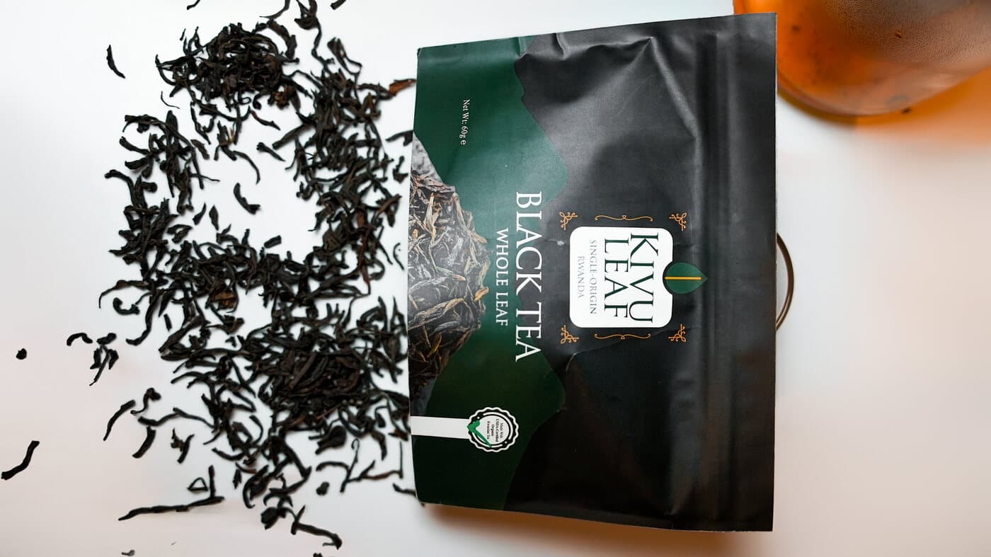 Overhead flat-lay of a KIVU Leaf Black Tea Whole Leaf pouch with loose tea leaves and a glass of brewed tea